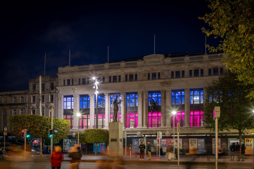 Nighttime building with vibrant blue and pink window lights, statue.