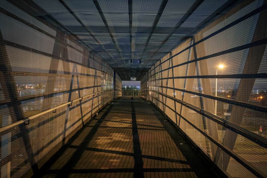 Nighttime view inside a mesh pedestrian bridge.