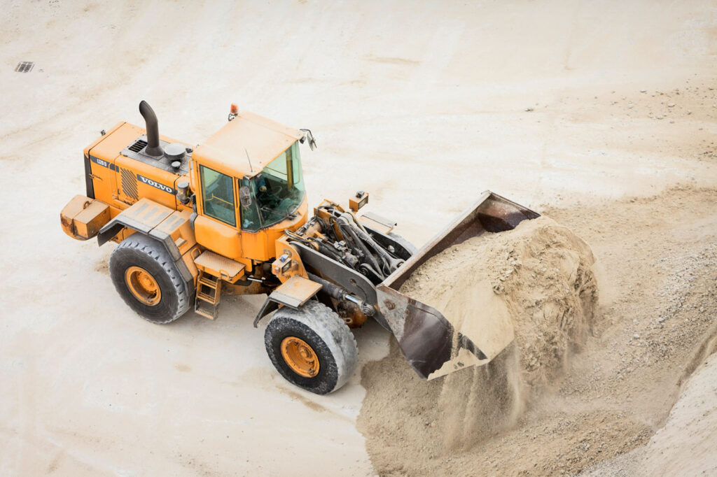 Orange Volvo loader moving sand at a construction site.