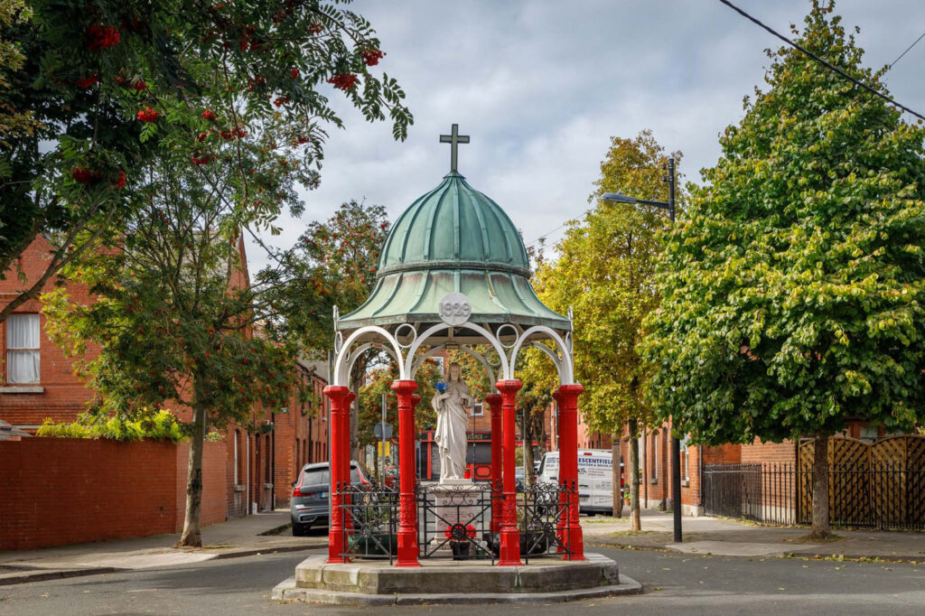 Ornate religious monument with statue on a tree-lined street.
