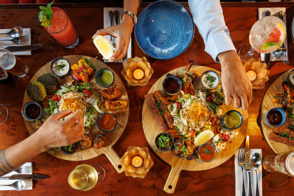 Overhead shot of hands sharing diverse Indian food and drinks.
