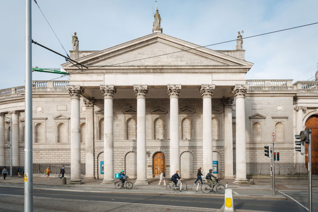 People and cyclists pass a grand classical building in Dublin.
