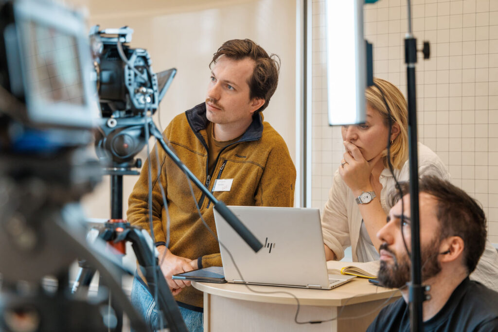 People discussing media production with camera and laptop.