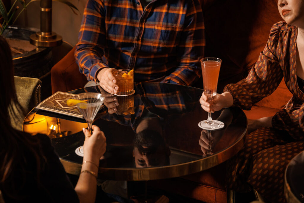 People enjoying cocktails at a stylish, dimly lit bar.