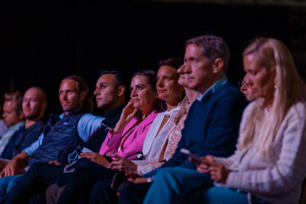 People in audience watching an event with focused expressions.