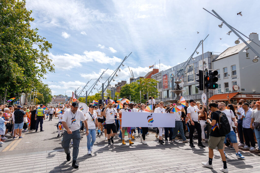 People marching in a Pride parade with an Apple banner.