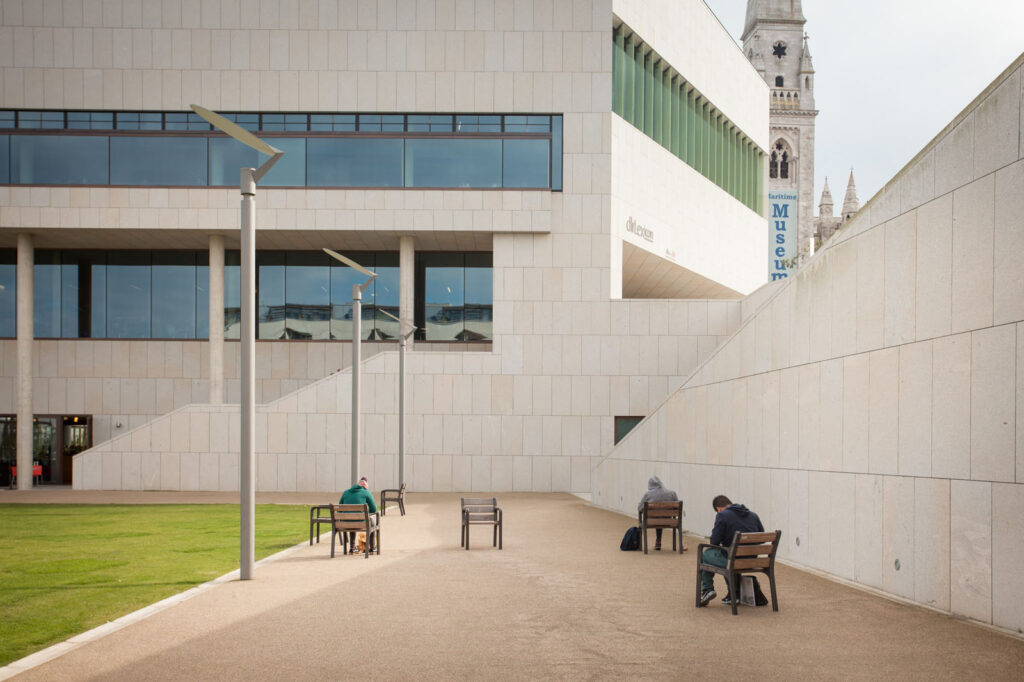 People sit on benches outside a modern museum and church.