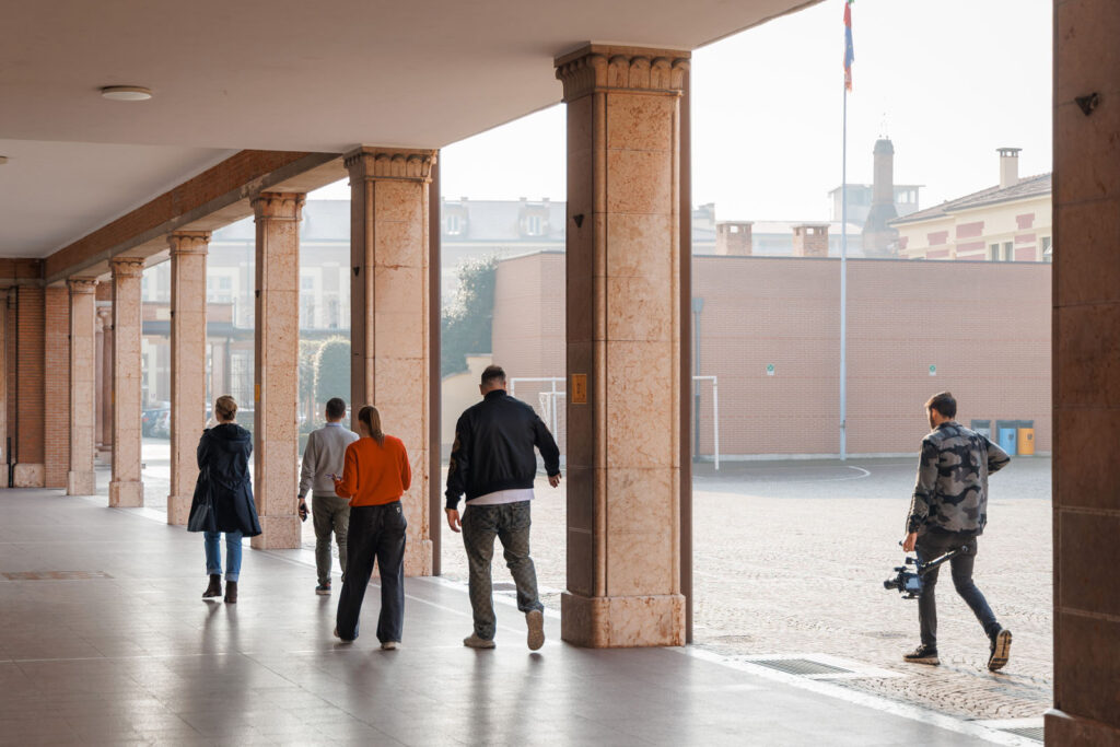 People walk under columns, one carries a camera.