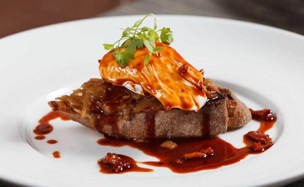 Poached egg on toast with caramelized onions and sauce.