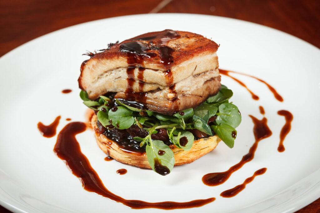 Pork belly with greens and sauce, beautifully presented.