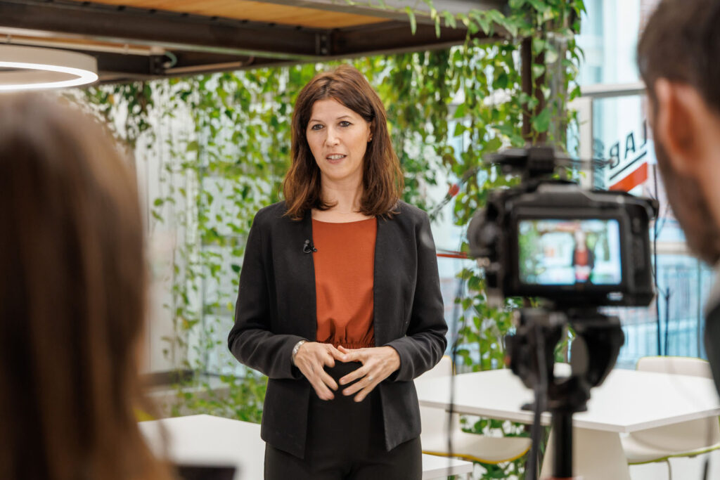 Professional woman speaks on camera in a modern office.