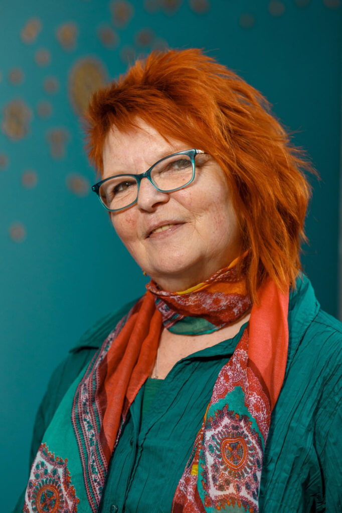 Red-haired woman in glasses and scarf smiles.