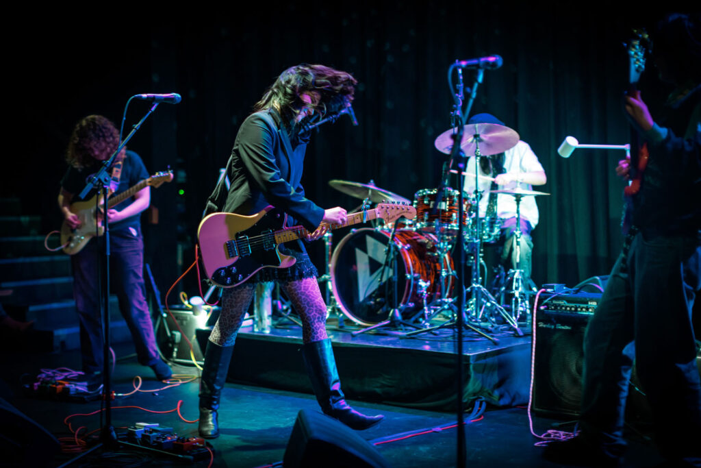 Rock band performing live under blue and purple lights.