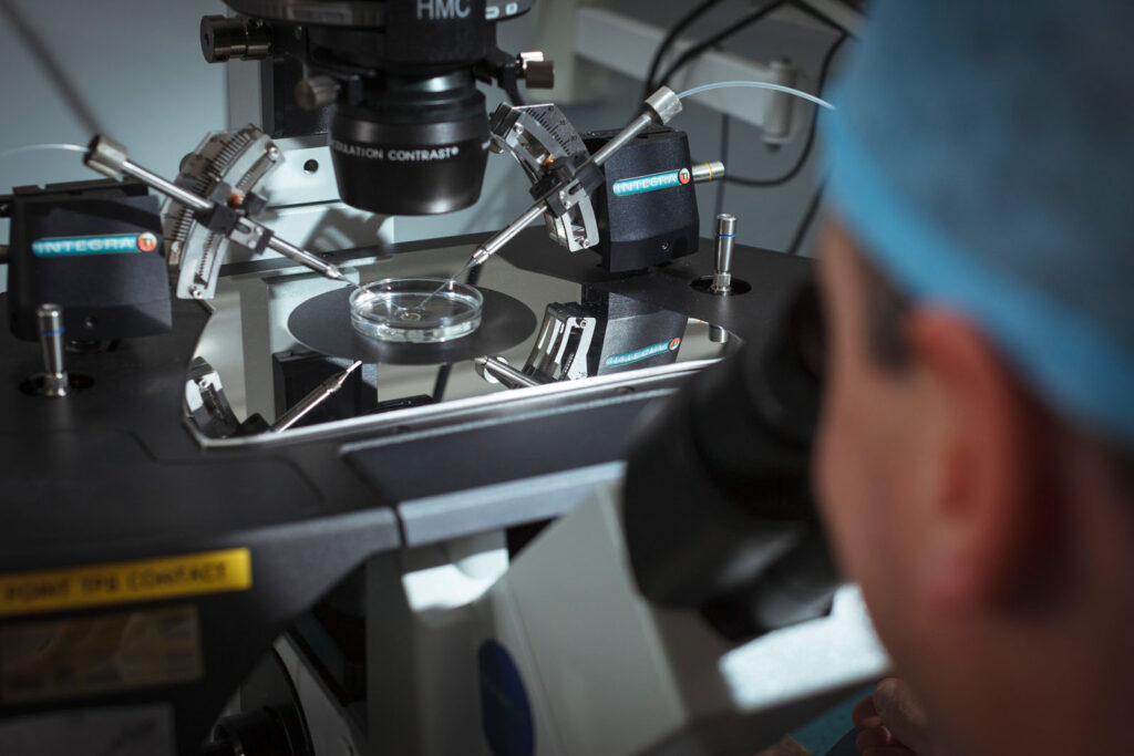 Scientist performing micro-manipulation under a microscope in a lab.