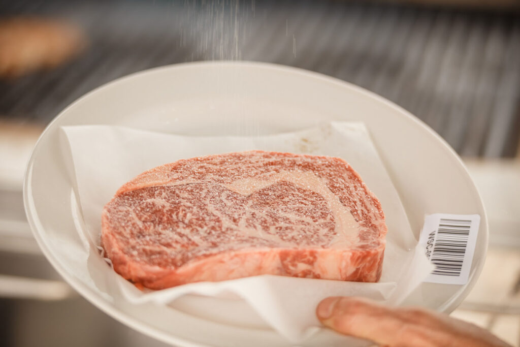 Seasoning a raw steak with salt.