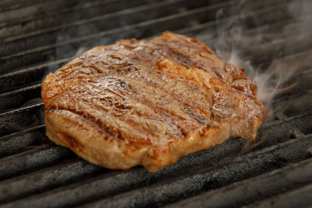 Sizzling steak on a grill, smoke rising.