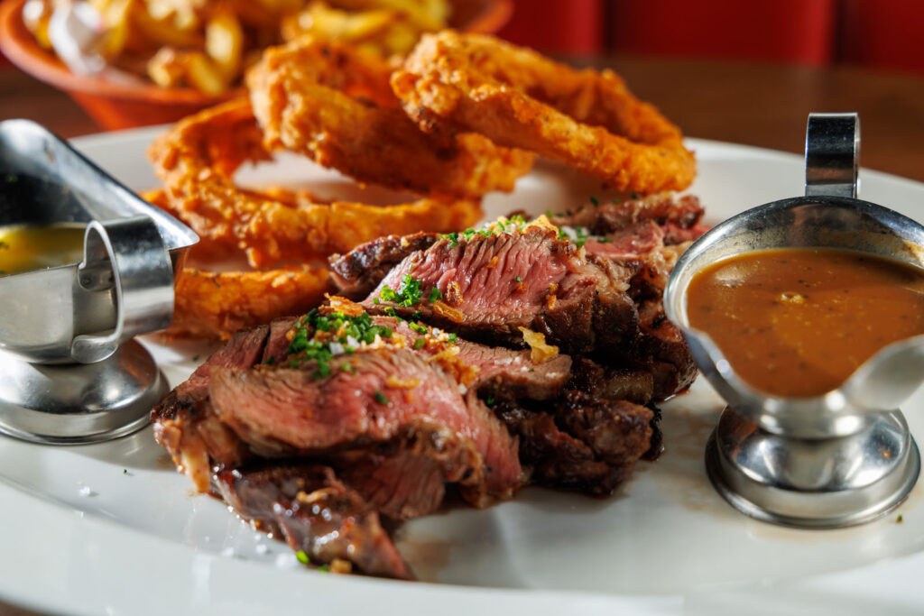Sliced steak with onion rings and sauces.