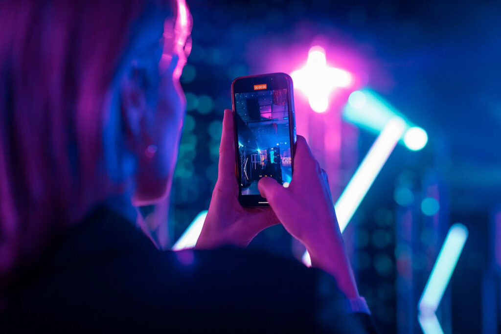 Smartphone records vibrant neon light display at event.