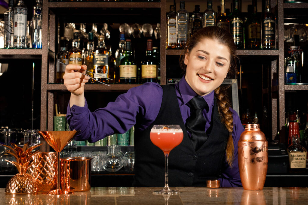 Smiling bartender preparing a cocktail at a well-stocked bar.