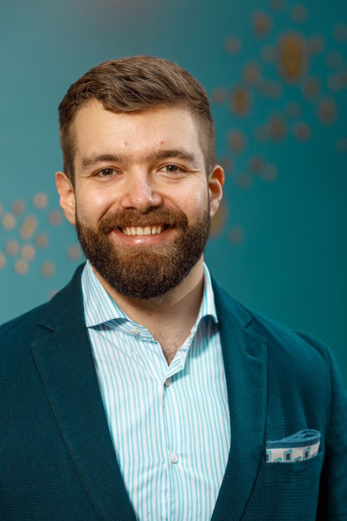 Smiling bearded man in jacket and striped shirt.