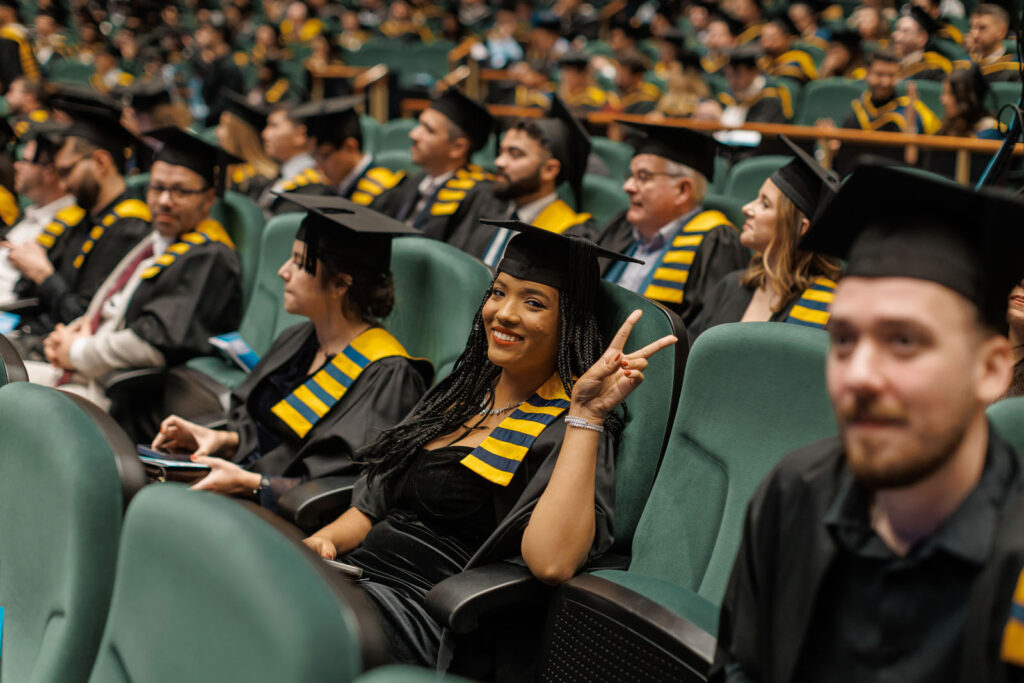 Smiling graduate makes peace sign at university ceremony.