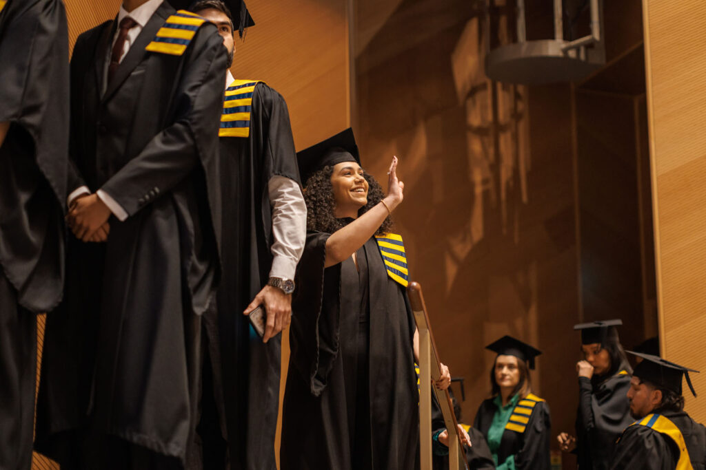 Smiling graduate waves during ceremony.