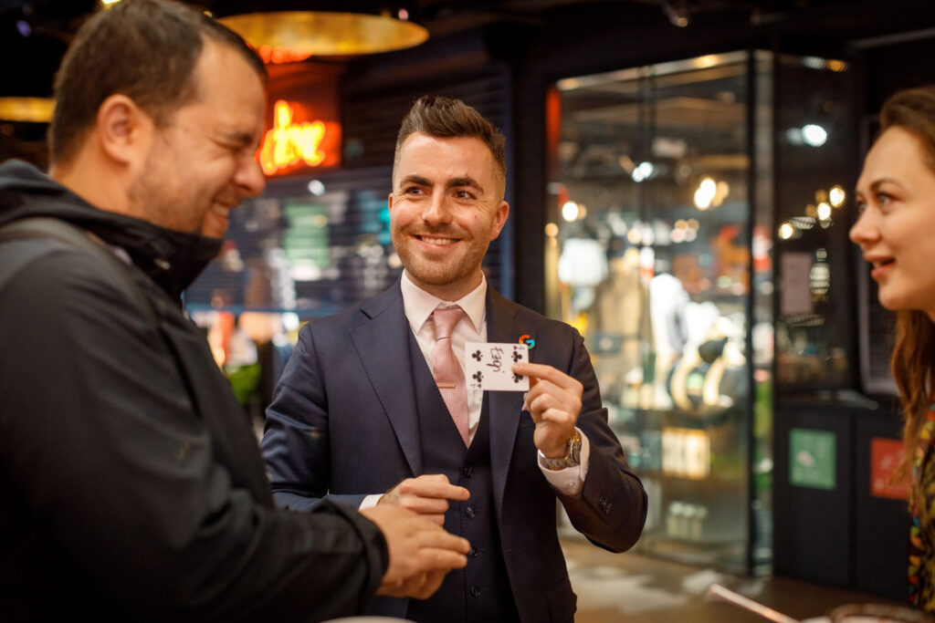 Smiling magician performs card trick for two people.