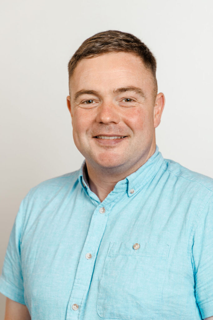Smiling man in blue shirt, headshot.