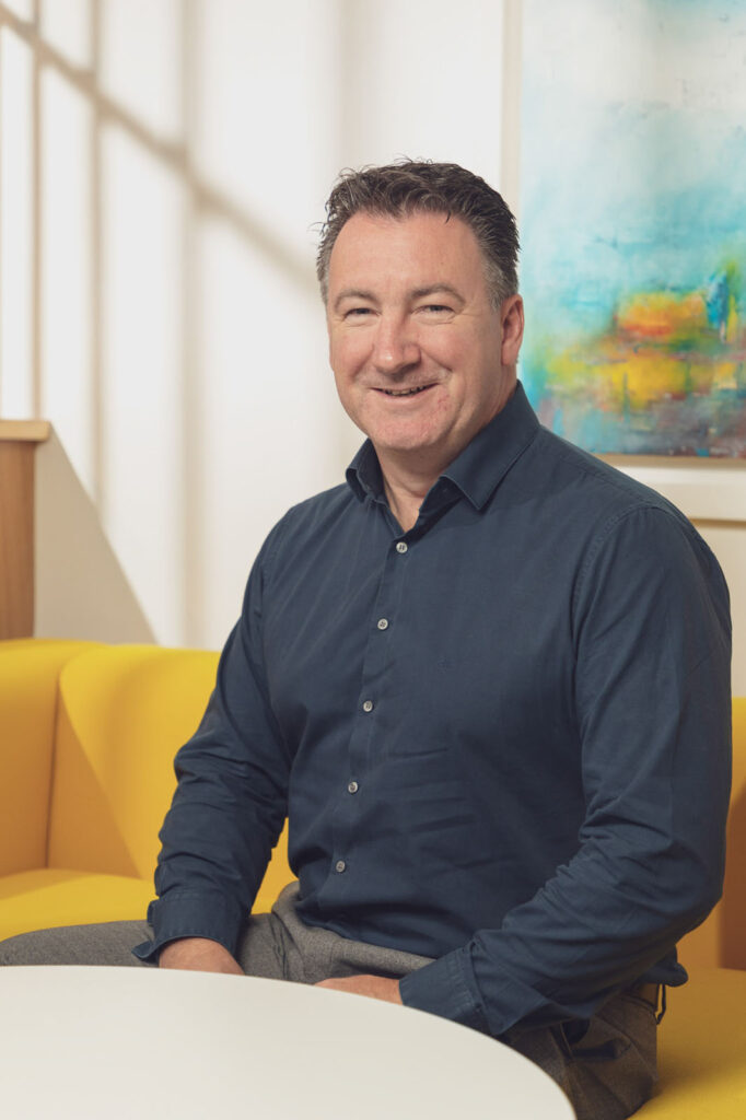 Smiling man in blue shirt on yellow couch.