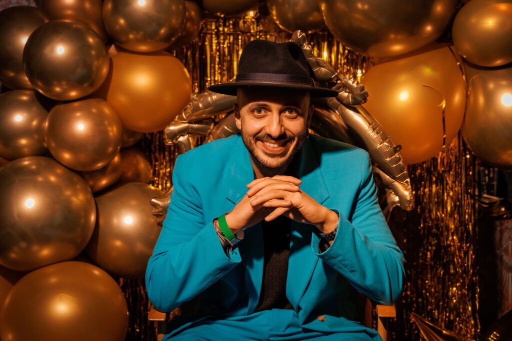Smiling man in blue suit and hat at a golden party.