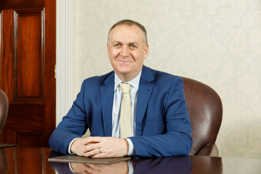 Smiling man in blue suit and tie at desk.