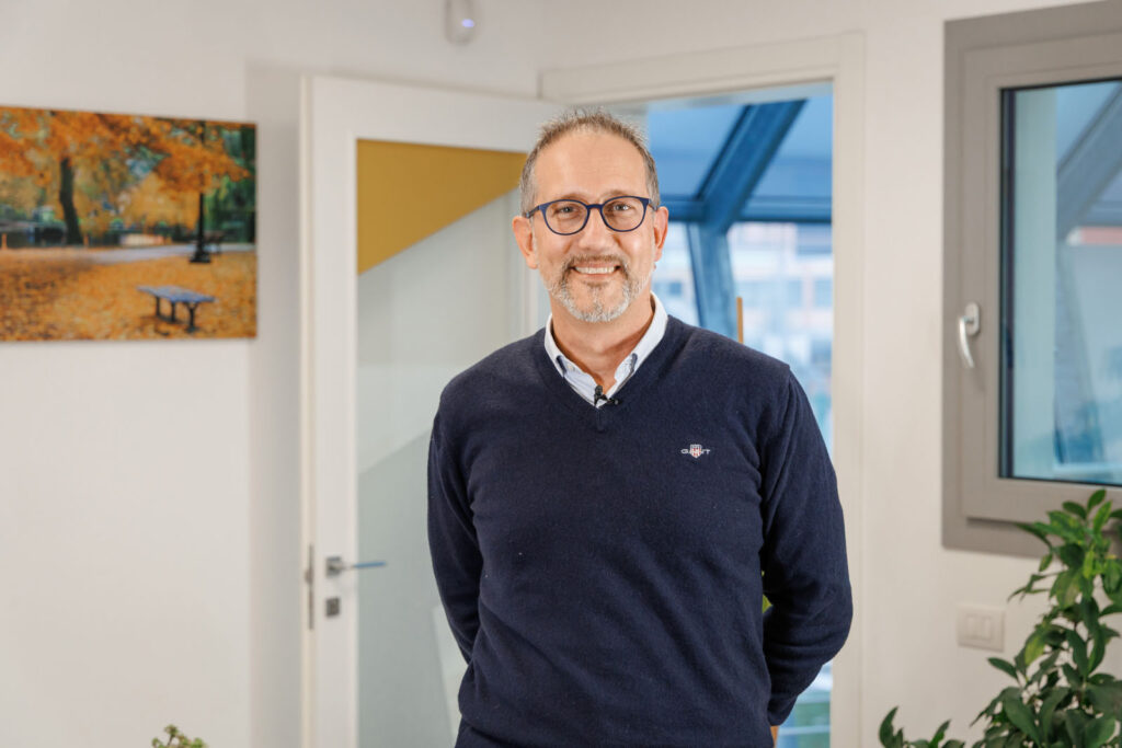 Smiling man in glasses and blue sweater standing indoors.