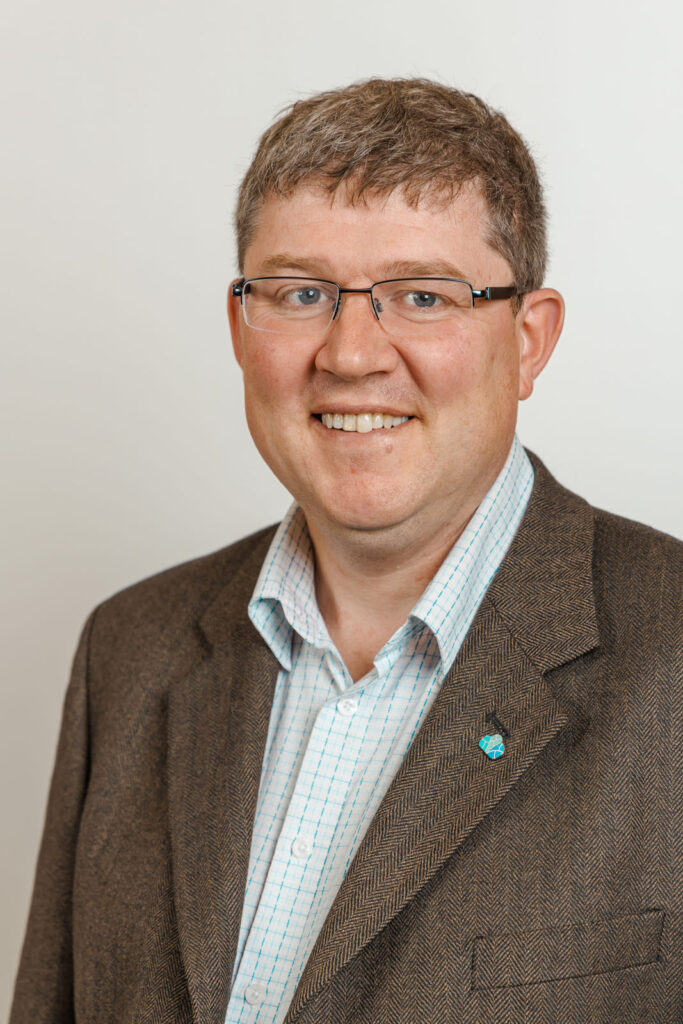 Smiling man in glasses and tweed jacket.