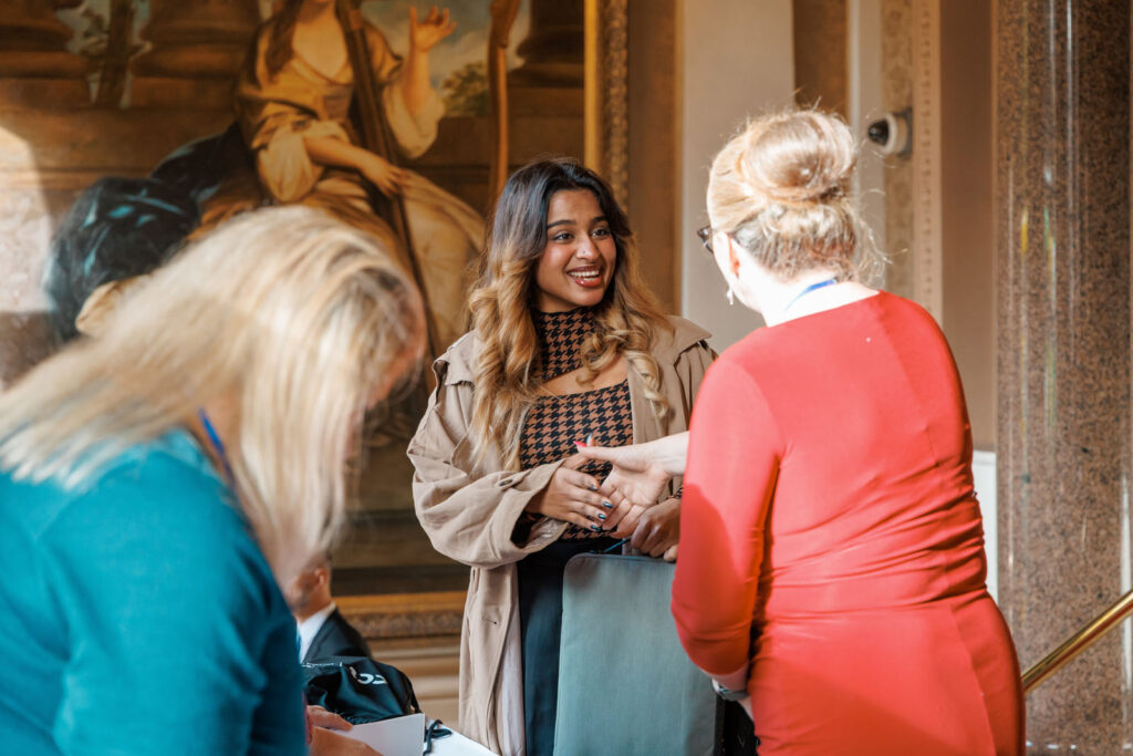 Smiling woman converses with another at an event.