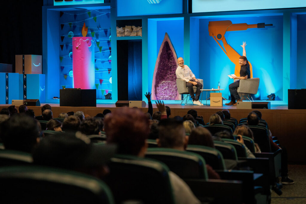 Speakers engage audience on a vibrant stage with Amazon branding.