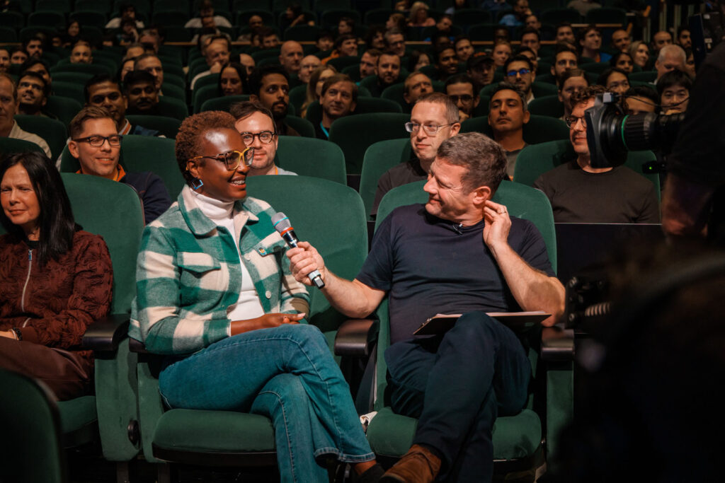 Speakers on stage, one with microphone, engaging audience.