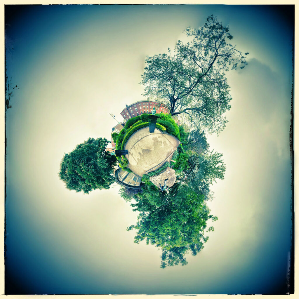 Spherical panorama of a green park with buildings and statue.