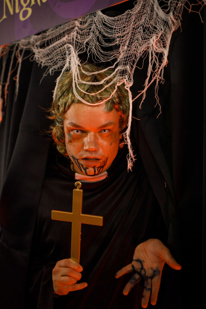 Spooky Halloween costume of a zombie priest holding a cross.