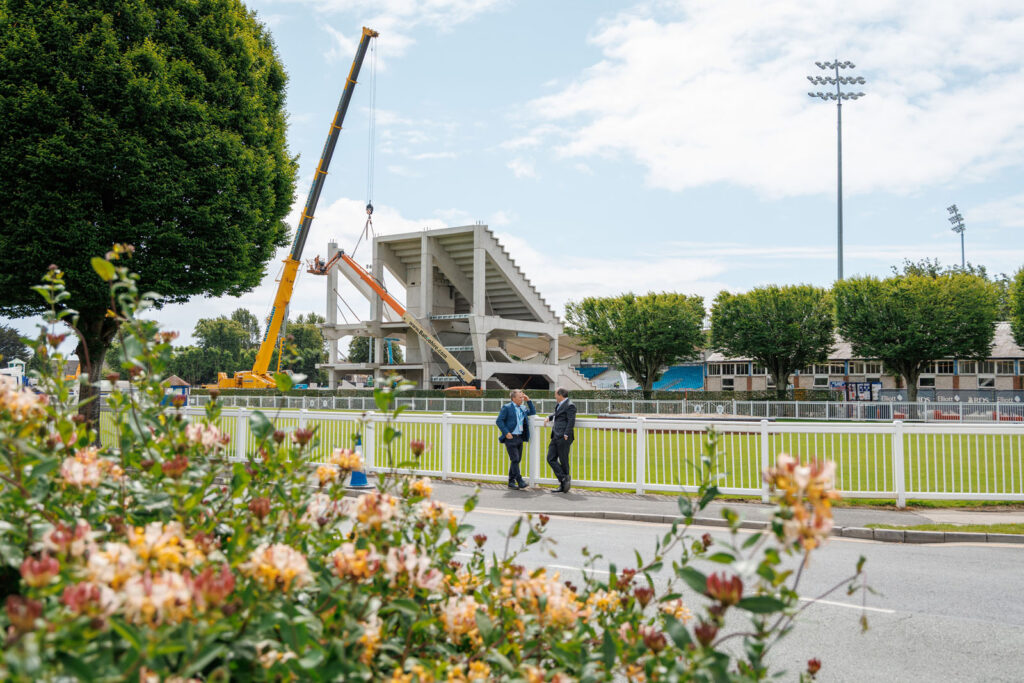 Stadium construction with crane, two men, and green racecourse.