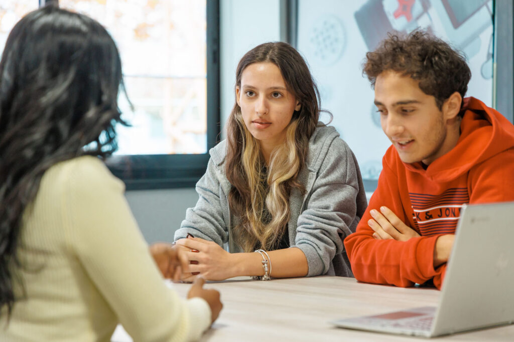 Students collaborating at a table with a laptop.