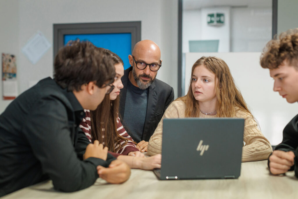 Teacher and students collaborate around a laptop.