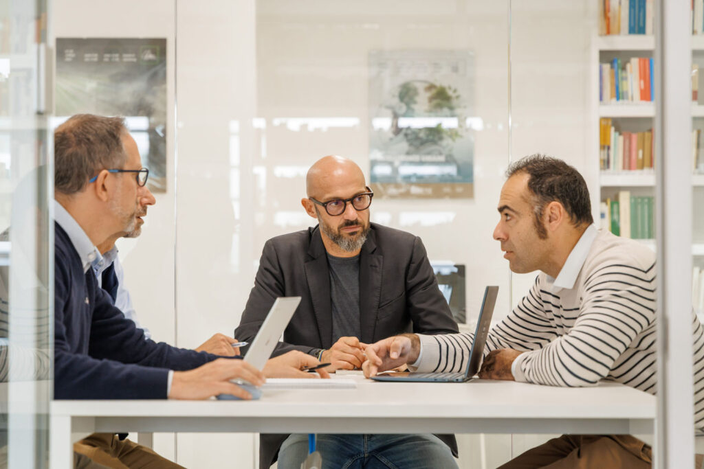 Three men collaborating at a table with laptops.