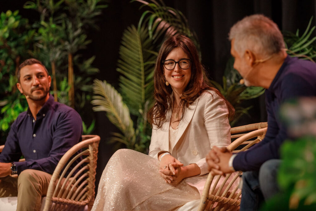 Three people on stage, woman smiling, engaging in discussion.