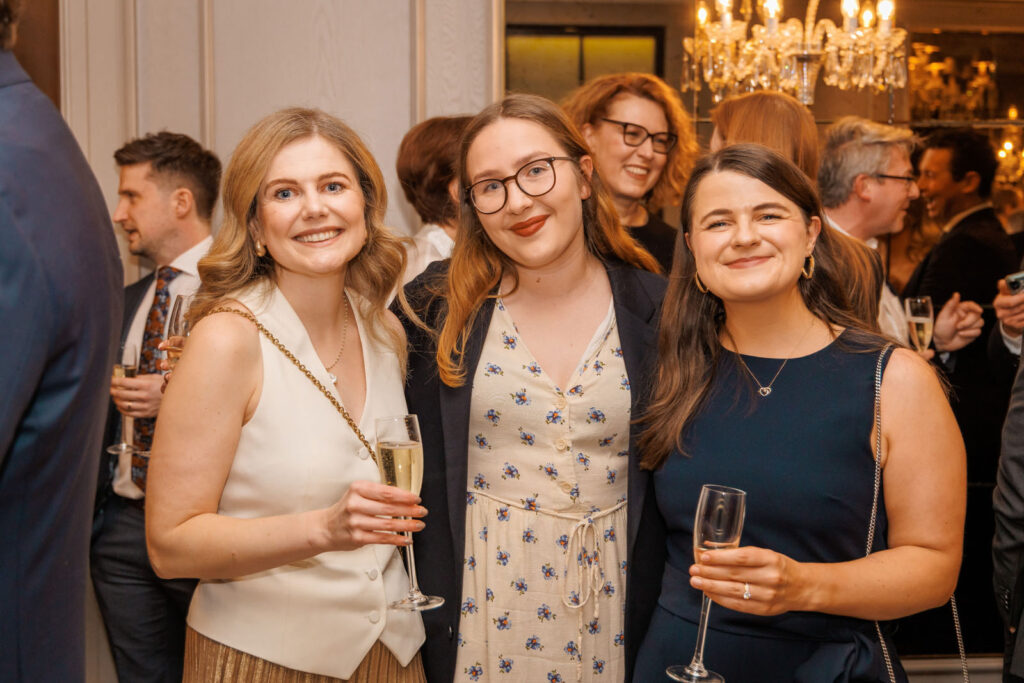 Three smiling women enjoying champagne at a social event.