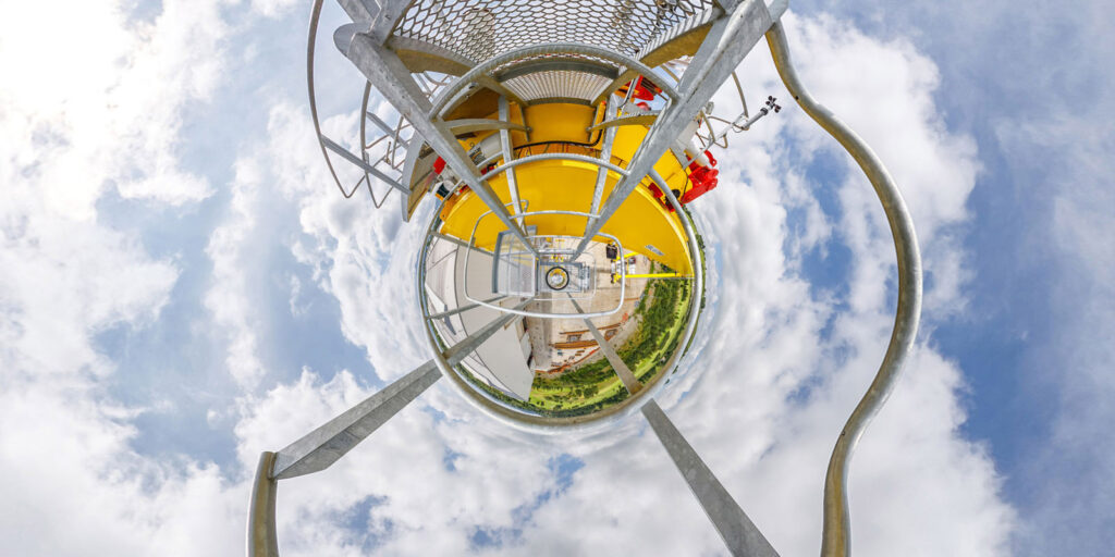 Tiny planet view from industrial structure under cloudy sky.