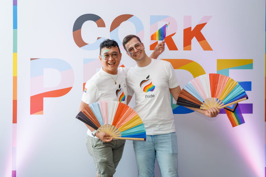 Two men celebrate Cork Pride with fans and flag.