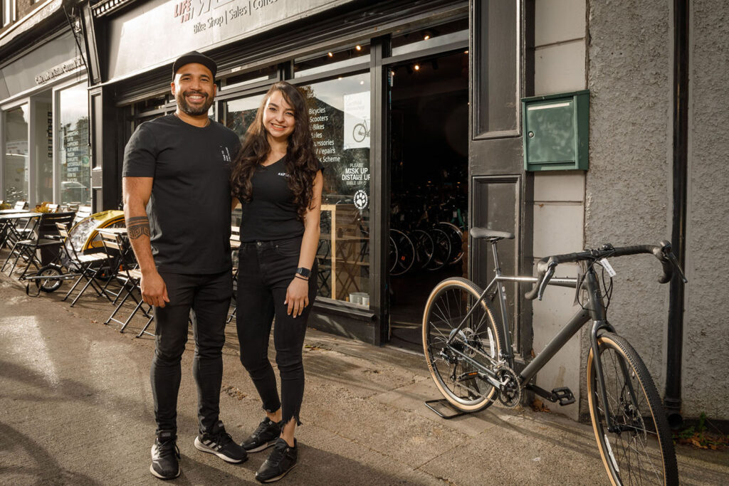 Two people smiling outside a bicycle shop.