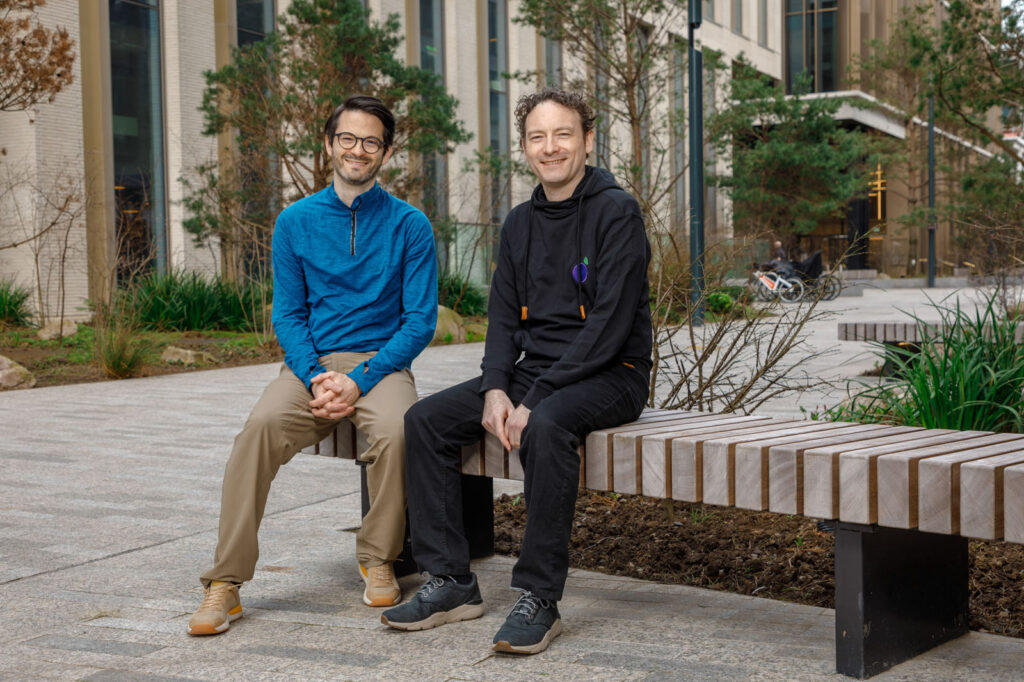 Two smiling men sitting on a bench.