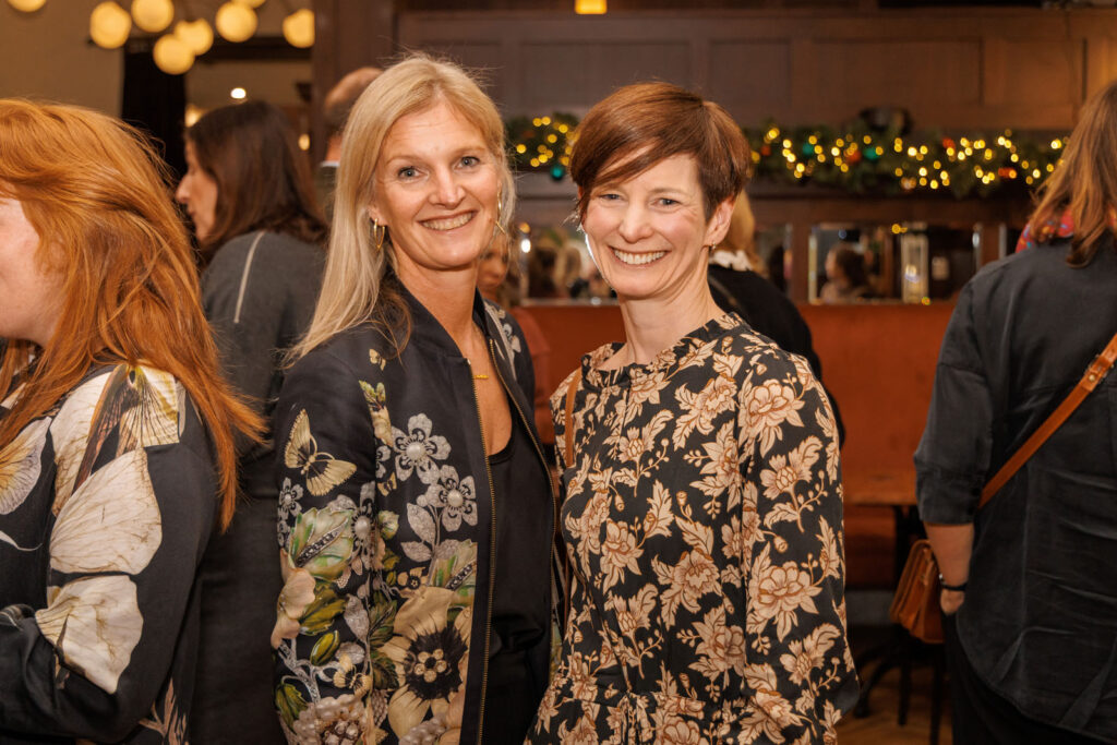 Two smiling women in patterned tops at an event.