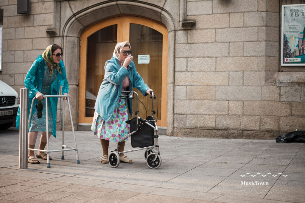 Two women with walkers and raincoats on a city street.